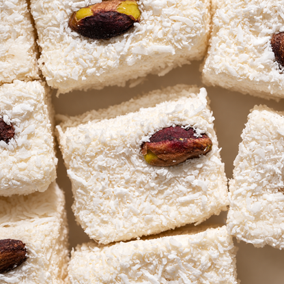 Close view of Classic Marshmallow cubes coated in coconut, each topped with a single pistachio.