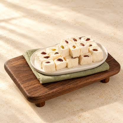 A platter of Classic Marshmallow cubes coated in coconut and topped with pistachios, on green linen and a wooden serving board.